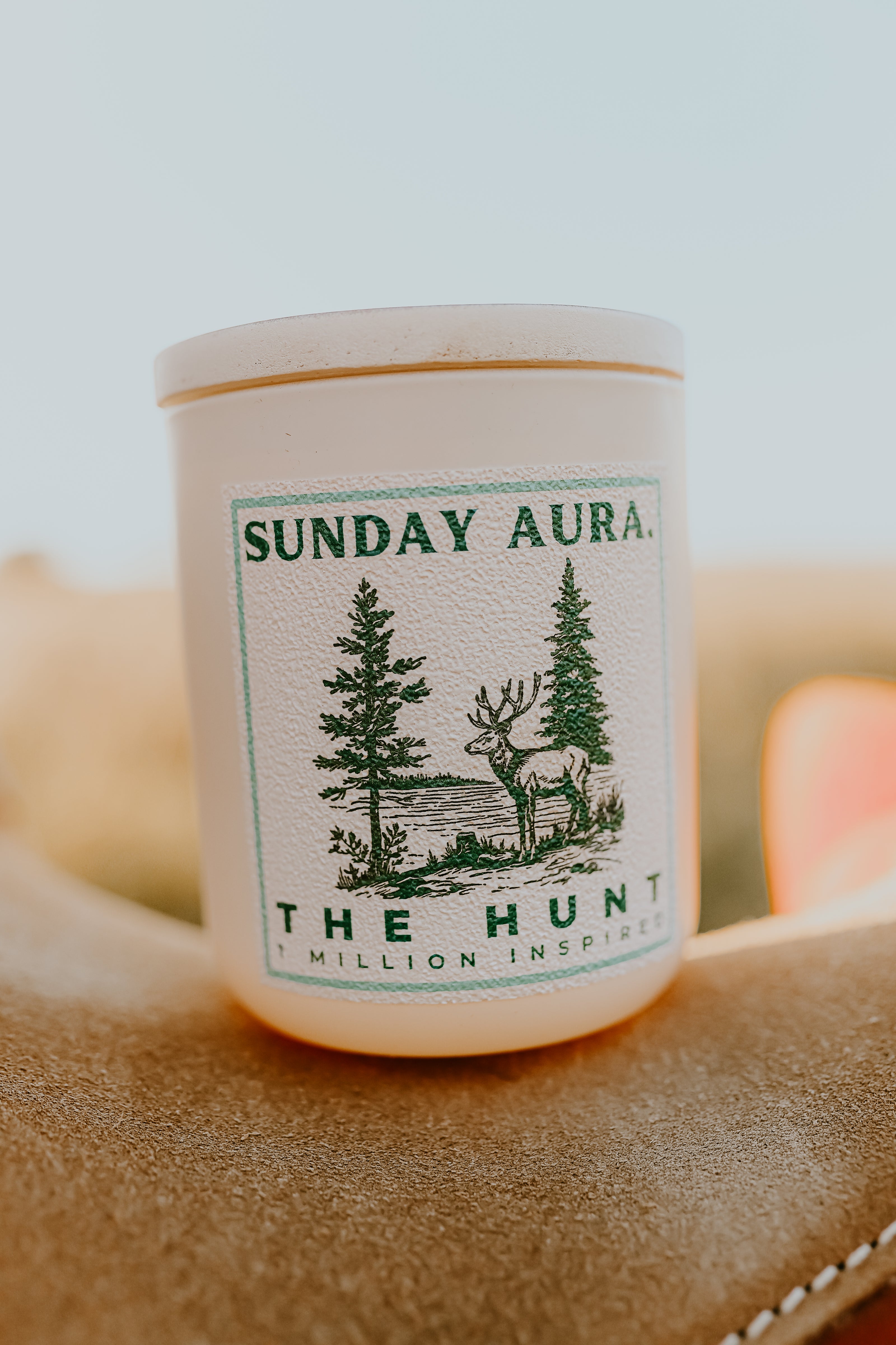 Candle with 'Sunday Aura' label featuring nature-themed design on a textured surface.