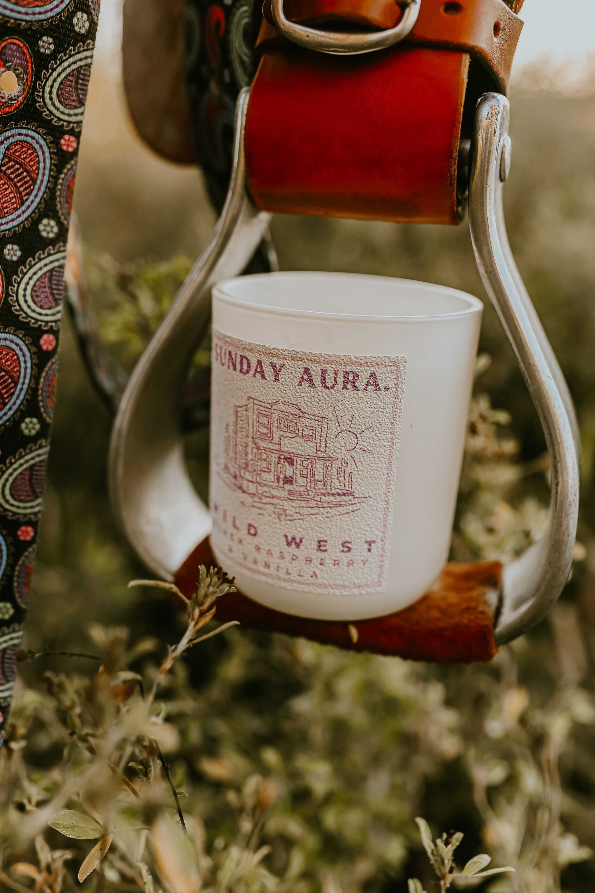 White candle with 'Sunday Aura' branding hanging from a leather strap against a natural background