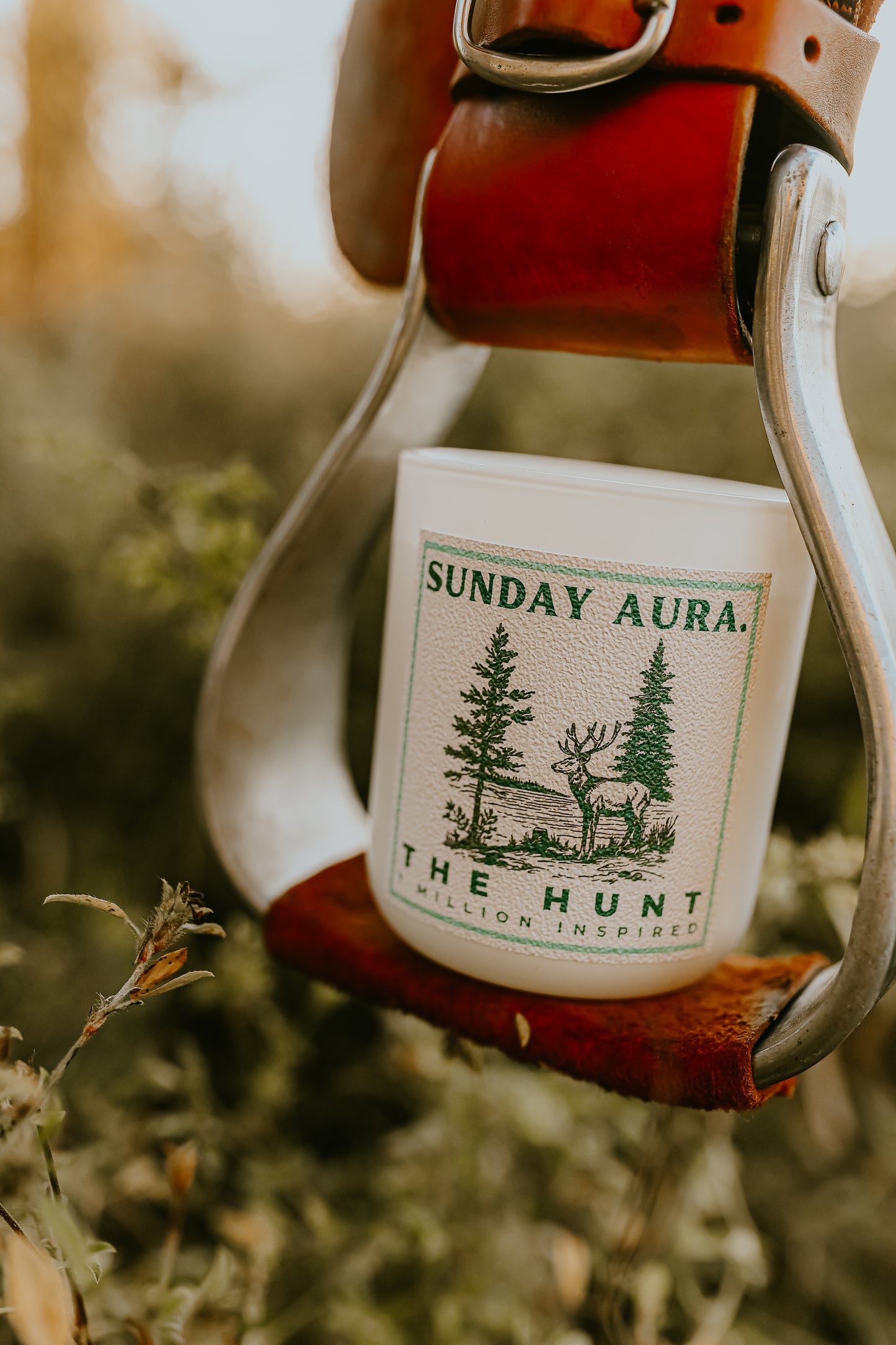 Candle labeled 'Sunday Aura' in a leather holder with a forest design on a natural background