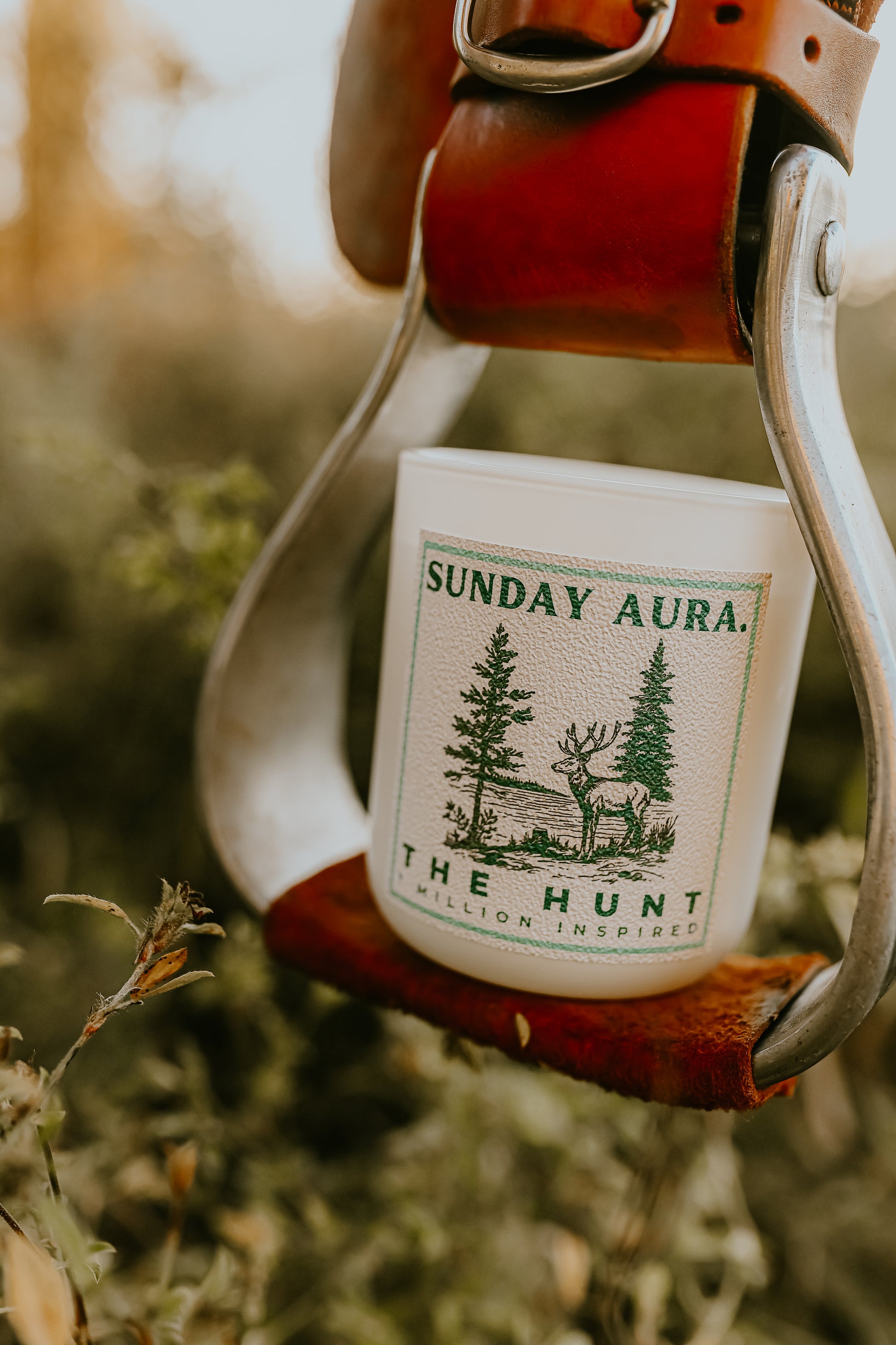 Candle labeled 'Sunday Aura' in a leather holder with a forest design on a natural background