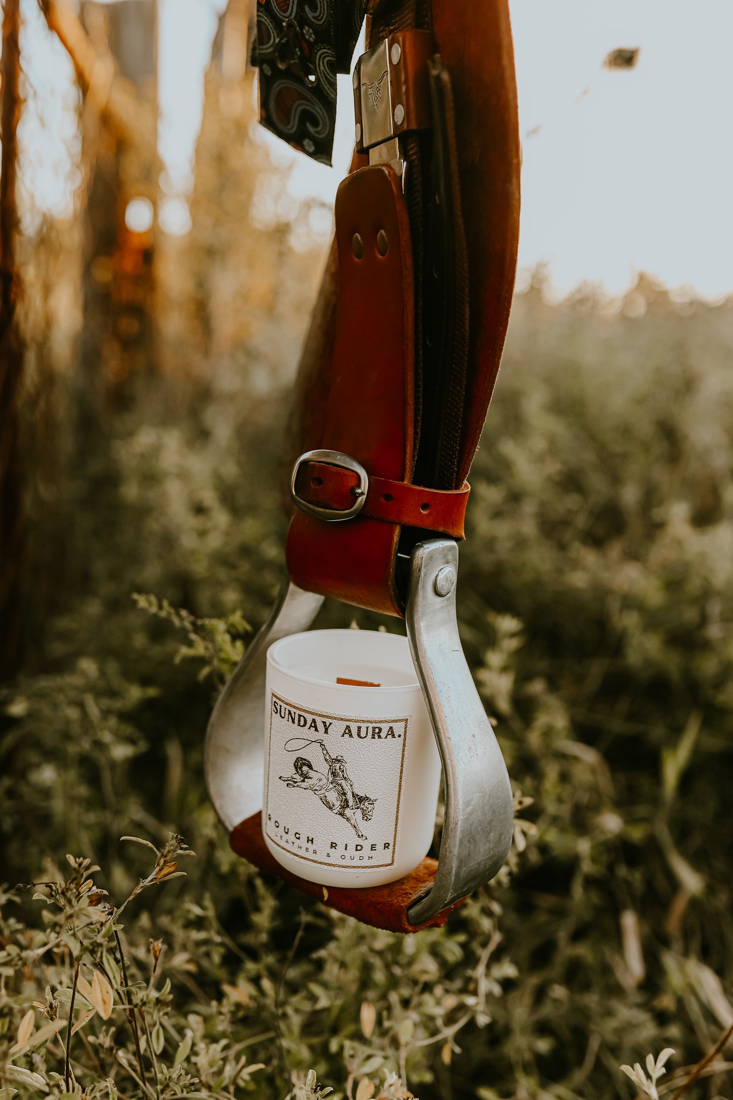 Bottle of Sunday Aurora Rye Whiskey hanging from a leather strap with a blurred natural background