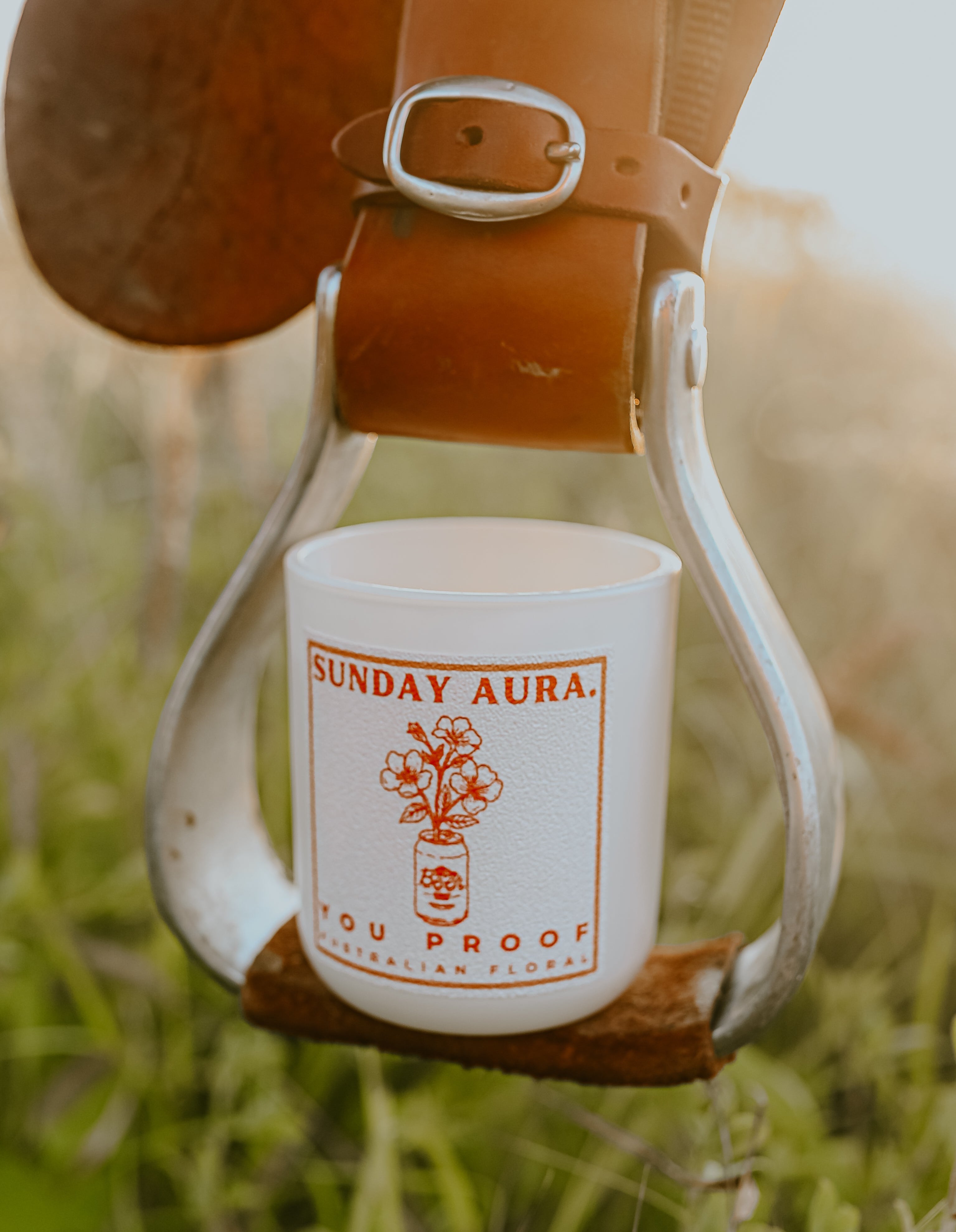 A white candle with red and green text, and a depiction of an animal, placed on a stirrup with a belt in an outdoor setting.