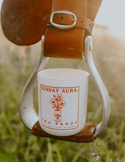 A white candle with red and green text, and a depiction of an animal, placed on a stirrup with a belt in an outdoor setting.