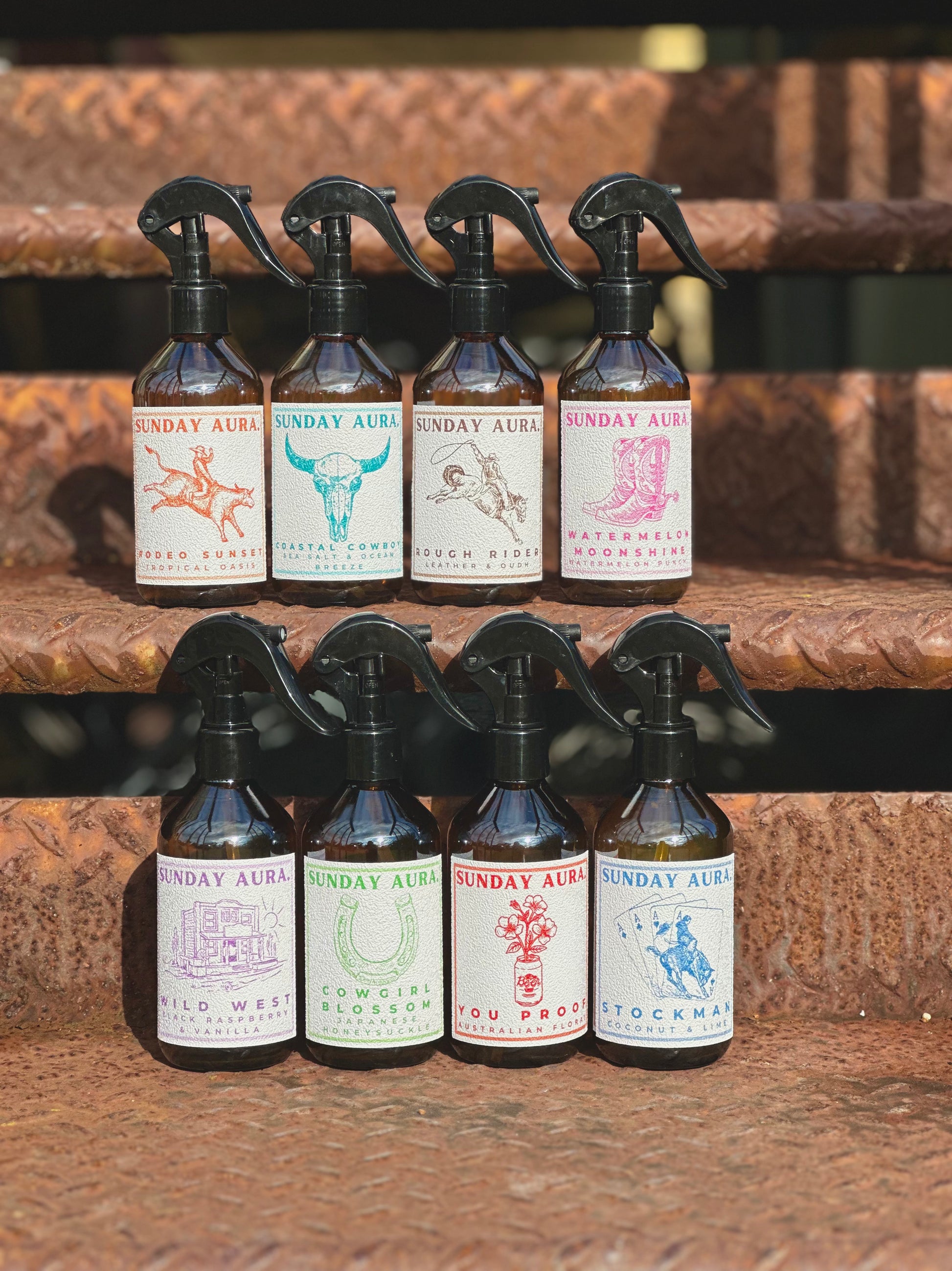 A series of Western-themed room spray bottles with labels featuring illustrations of animals and fronts, arranged on a wooden surface.